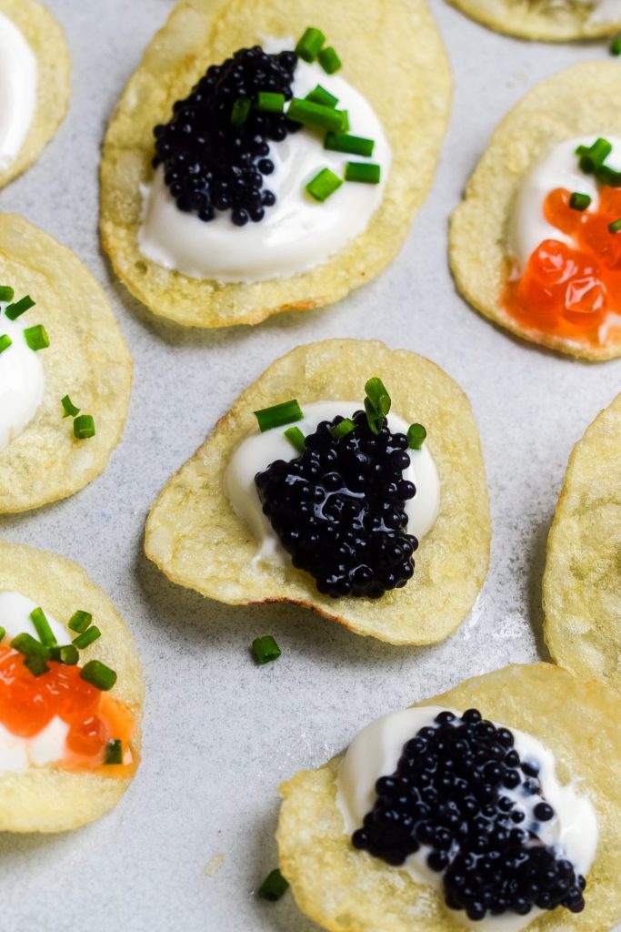 Close up of a potato chip topped with sour cream, caviar and chives.