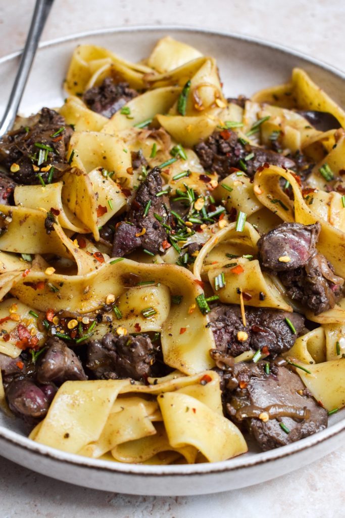 Close up of a chicken liver and rosemary pappardelle in a brown bowl