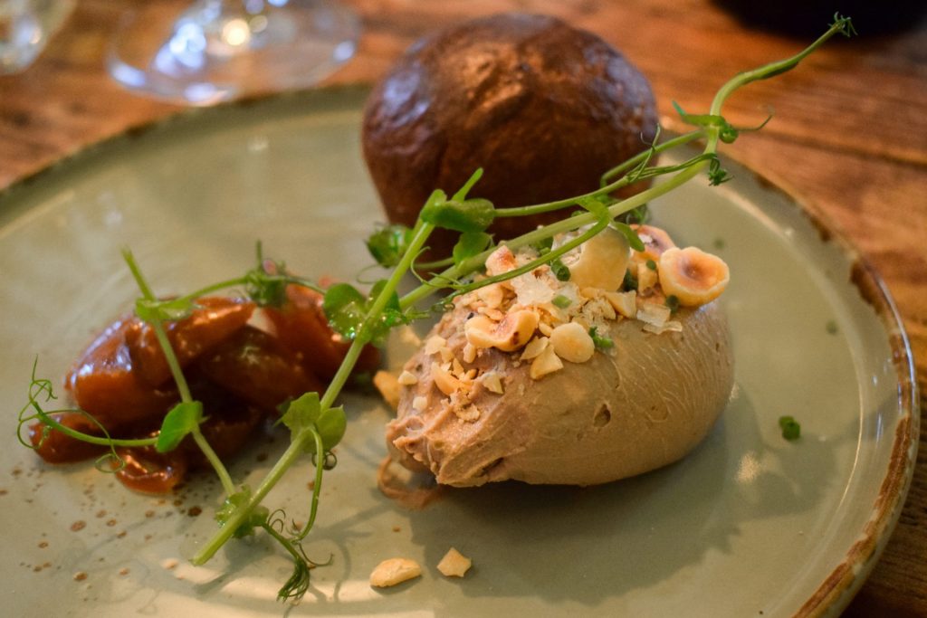 Quenelle of duck liver parfait topped with pea shoots and hazelnuts with a brioche muffin and chutney on the side.