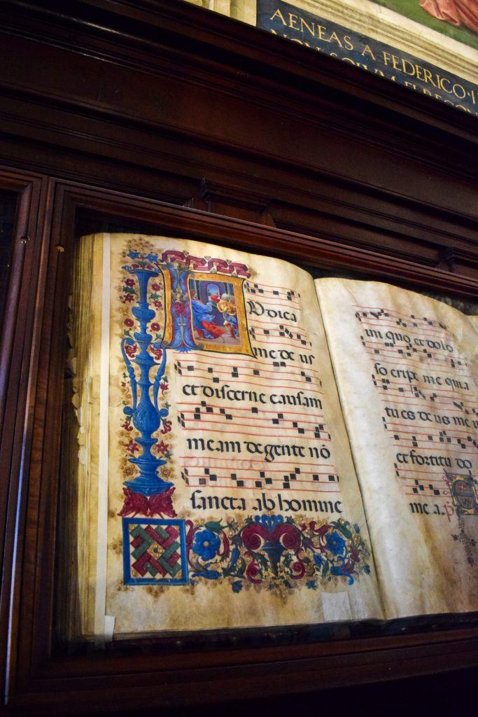 Medieval illuminated music manuscript in a glass display case.