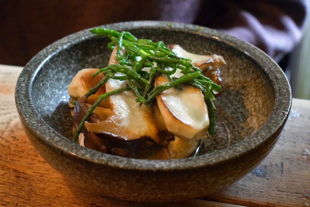 Sliced king oyster mushrooms in a grey bowl topped with samphire.