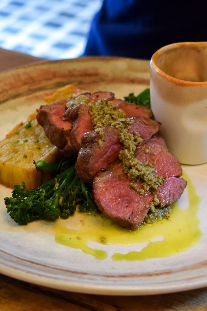 Sliced lamb topped with a green sauce on a white plate.