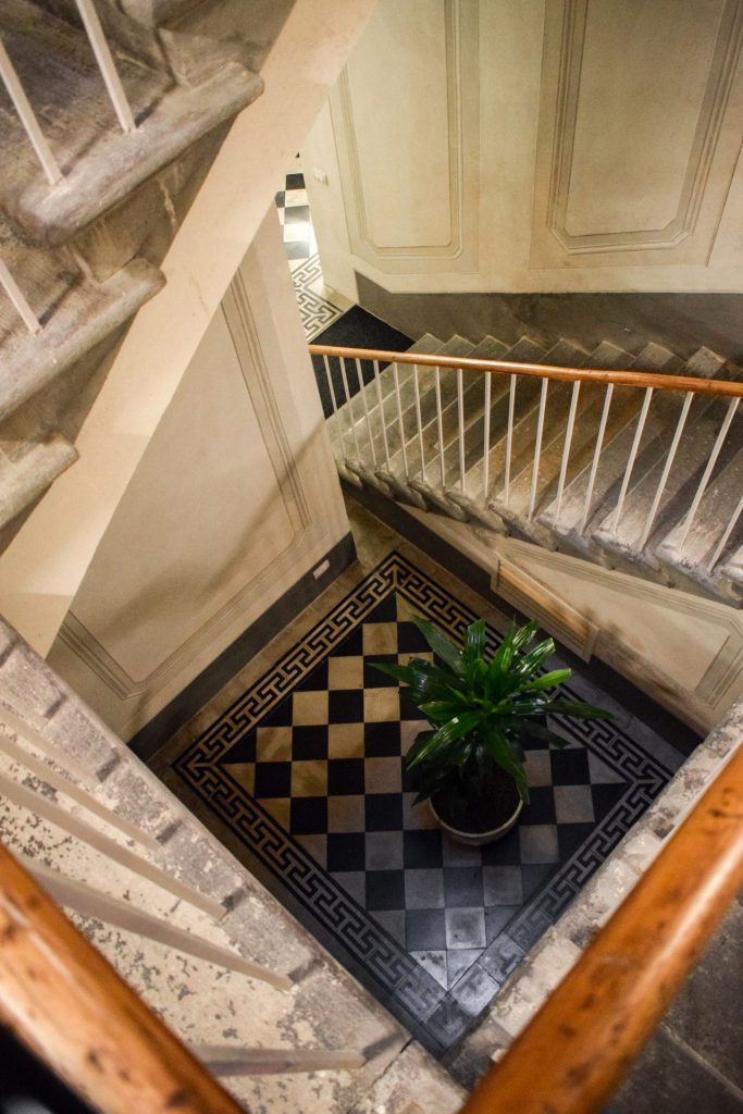 View to a black and white tiled floor and a pot plant down the stairwell at Palazzo Feroci