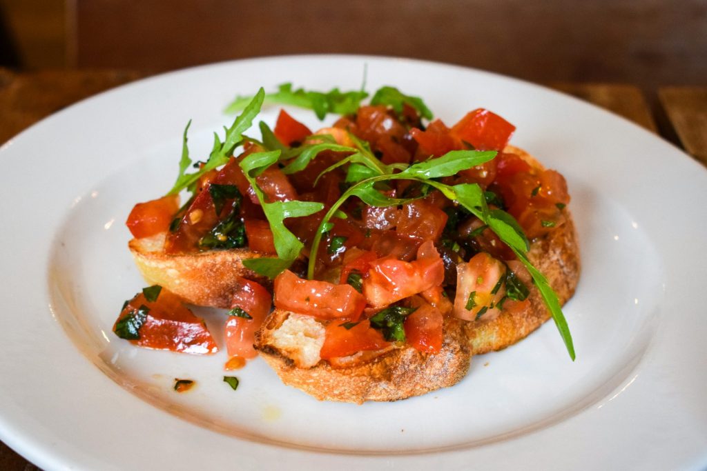 Bruschetta topped with rocket on a white plate.