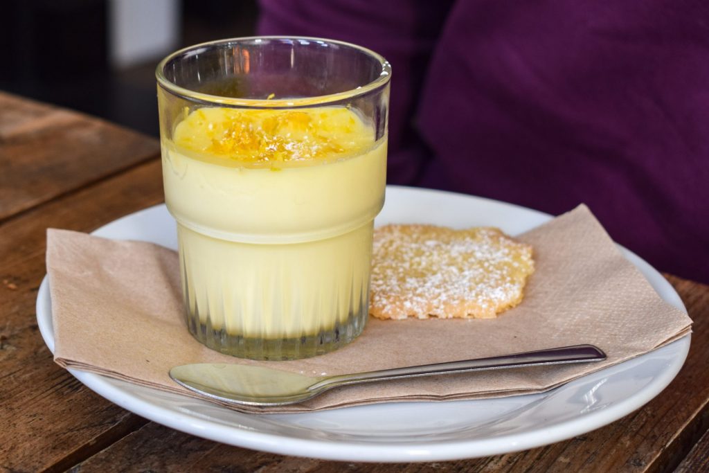 Lemon posset on a white plate next to a thin round of shortbread.
