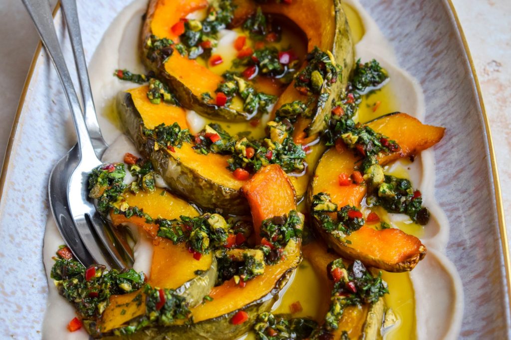Close up of a platter of squash wedges topped with salsa verde and chopped chilli.