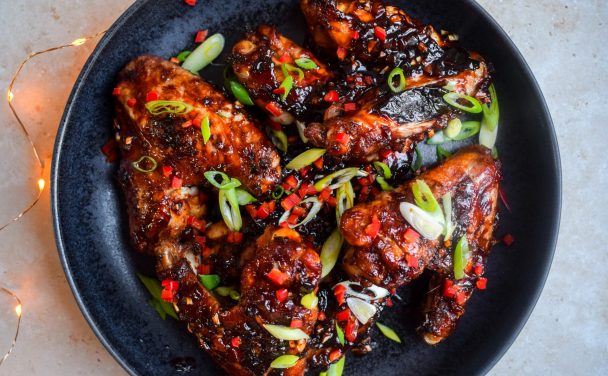 Sticky Asian Stem Ginger Chicken Wings on a black plate scattered with copped chilli and spring onions.