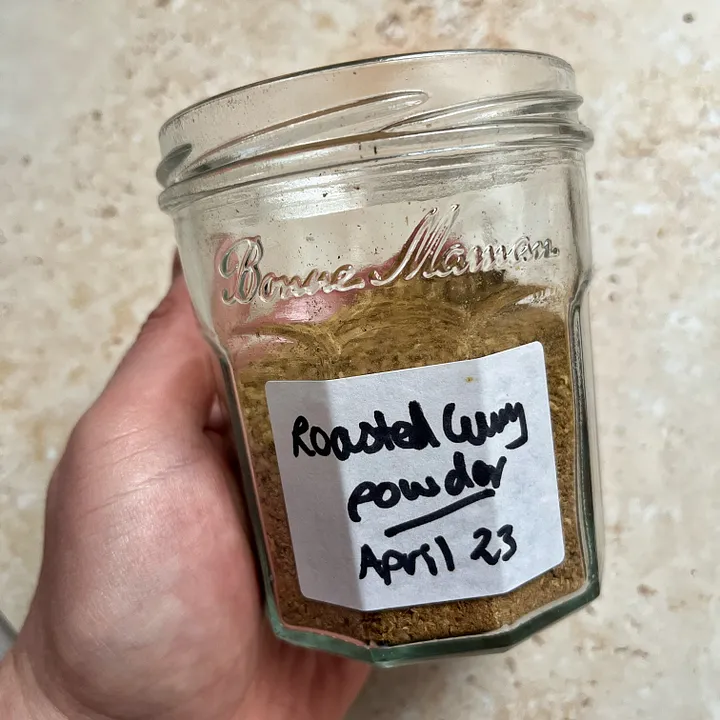 Hand holding a hand labeled jar of Roasted Curry Powder.
