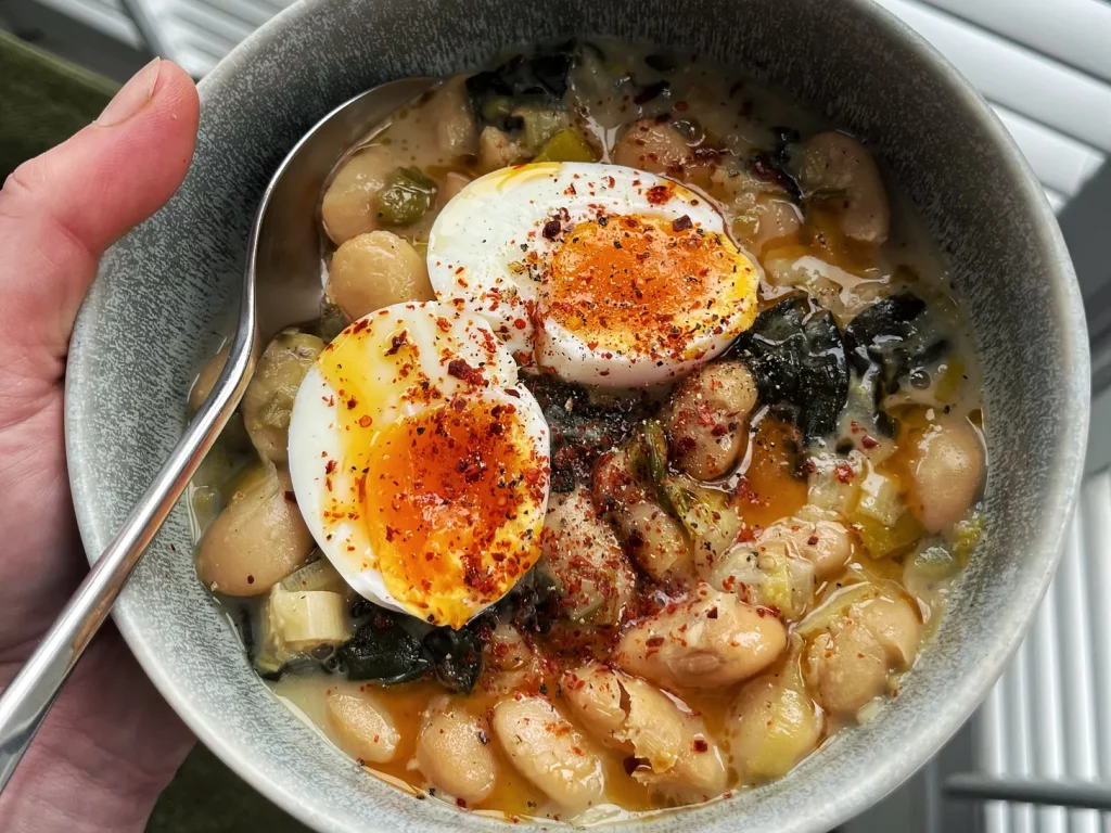 A bowl of butter bean and spinach stew with a jammy egg.