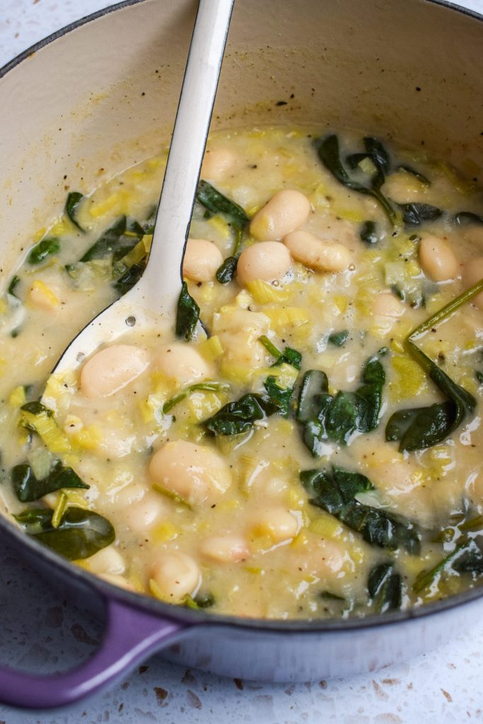 Close up of a butter bean, spinach and leek stew being spooned out of the cooking pot. 