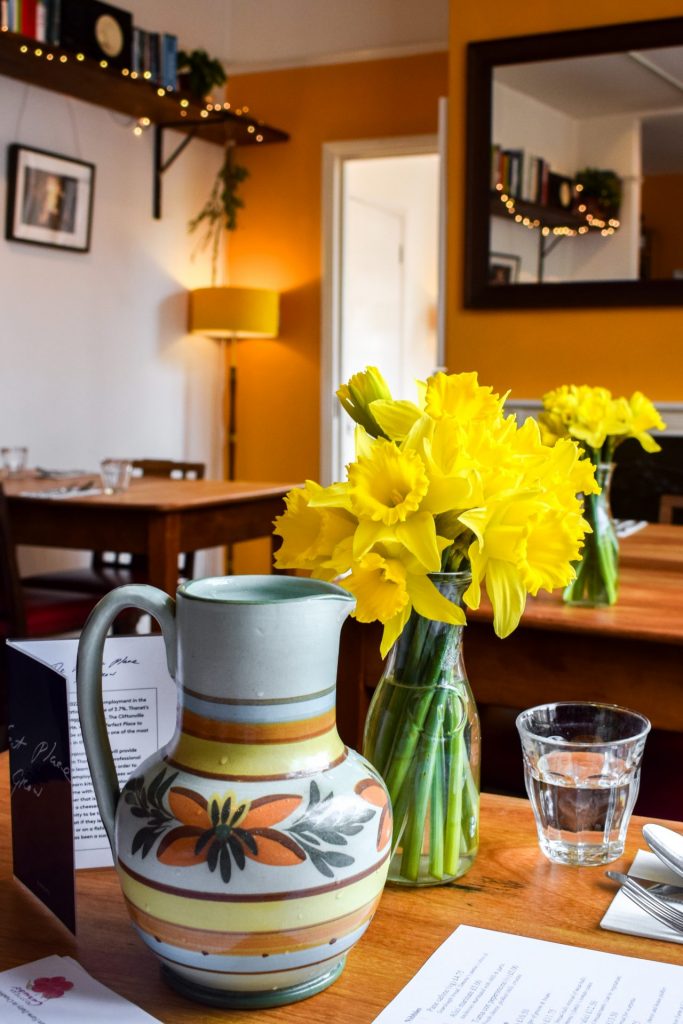 A water jug and a vase of daffodils on the table at Bottaga Caruso.