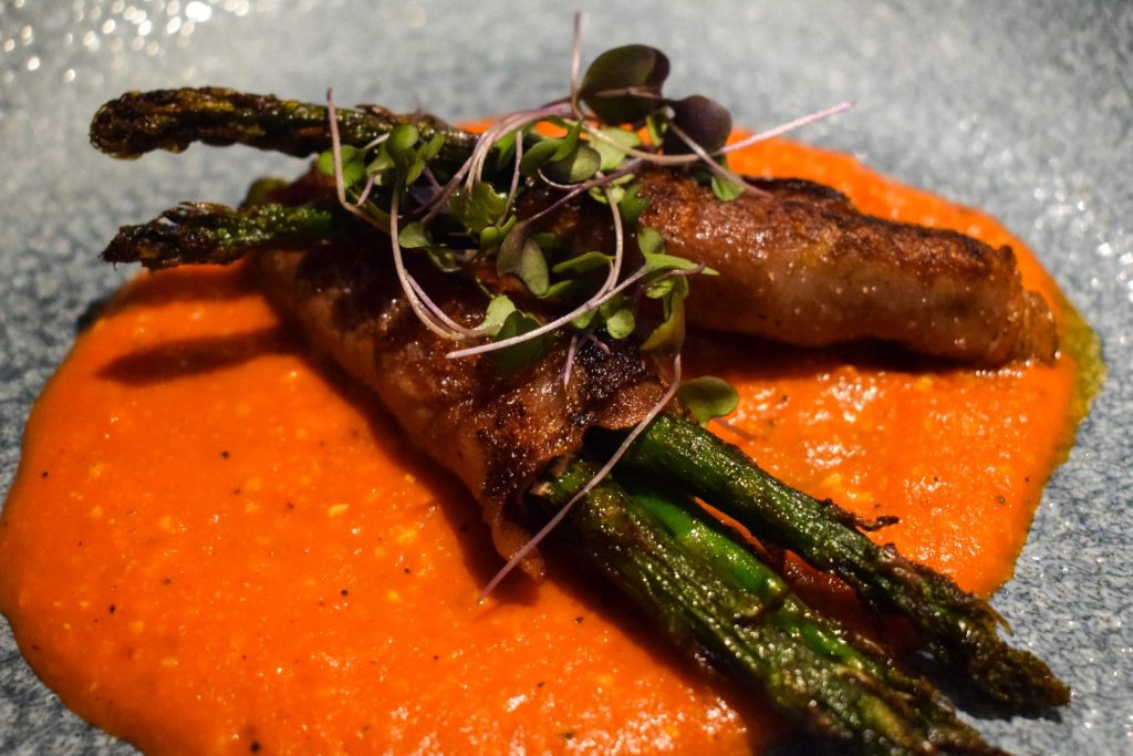 Charred asparagus wrapped in parma ham on top of a puddle of romesco sauce.