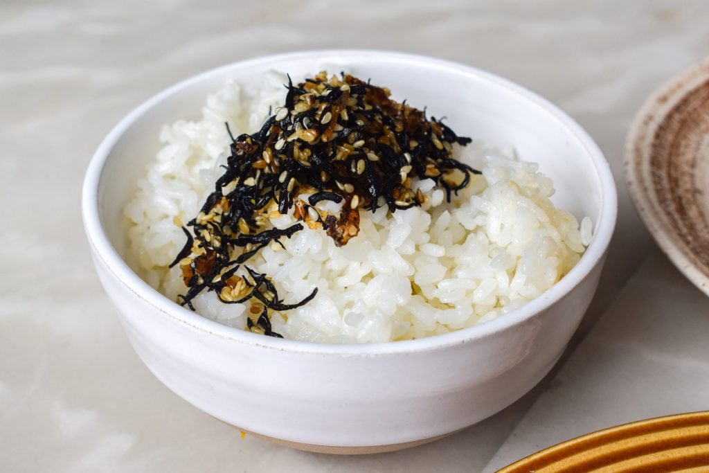 White bowl of rice topped with ferments and sesame seeds.