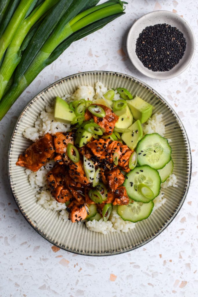 White bowl of spicy trout, rice, cucumber and avocado.