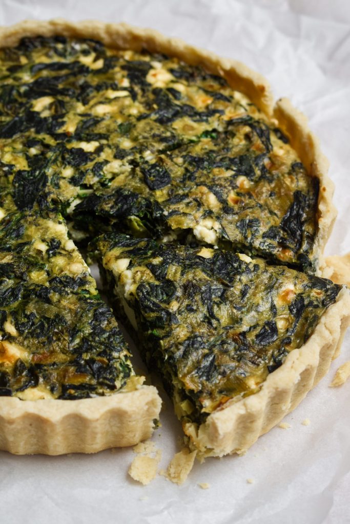 Close up of a slice being removed from a spinach and feta tart.