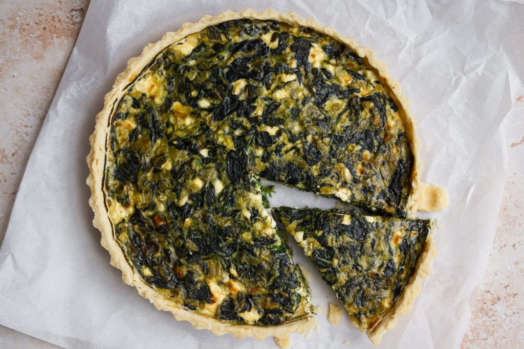 Overhead of a spanakopita tart with a slice taken out.