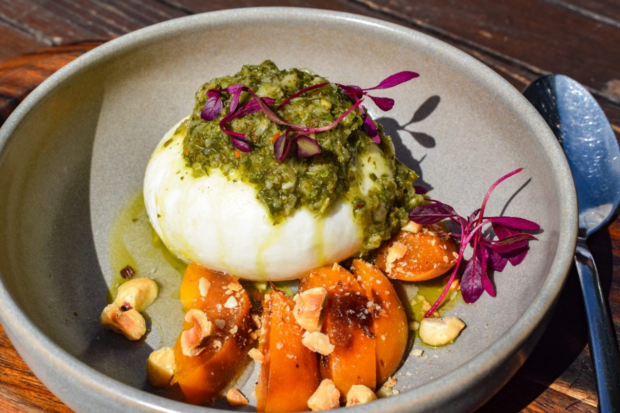 Burrata topped with chimmicuri sauce next to grilled apricot slices.