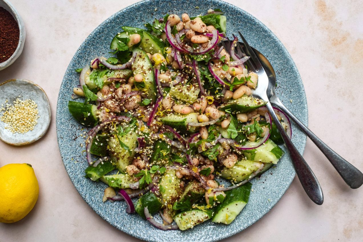 A salad of cucumber, white beans, red onions and sesame seeds on a blue plate.