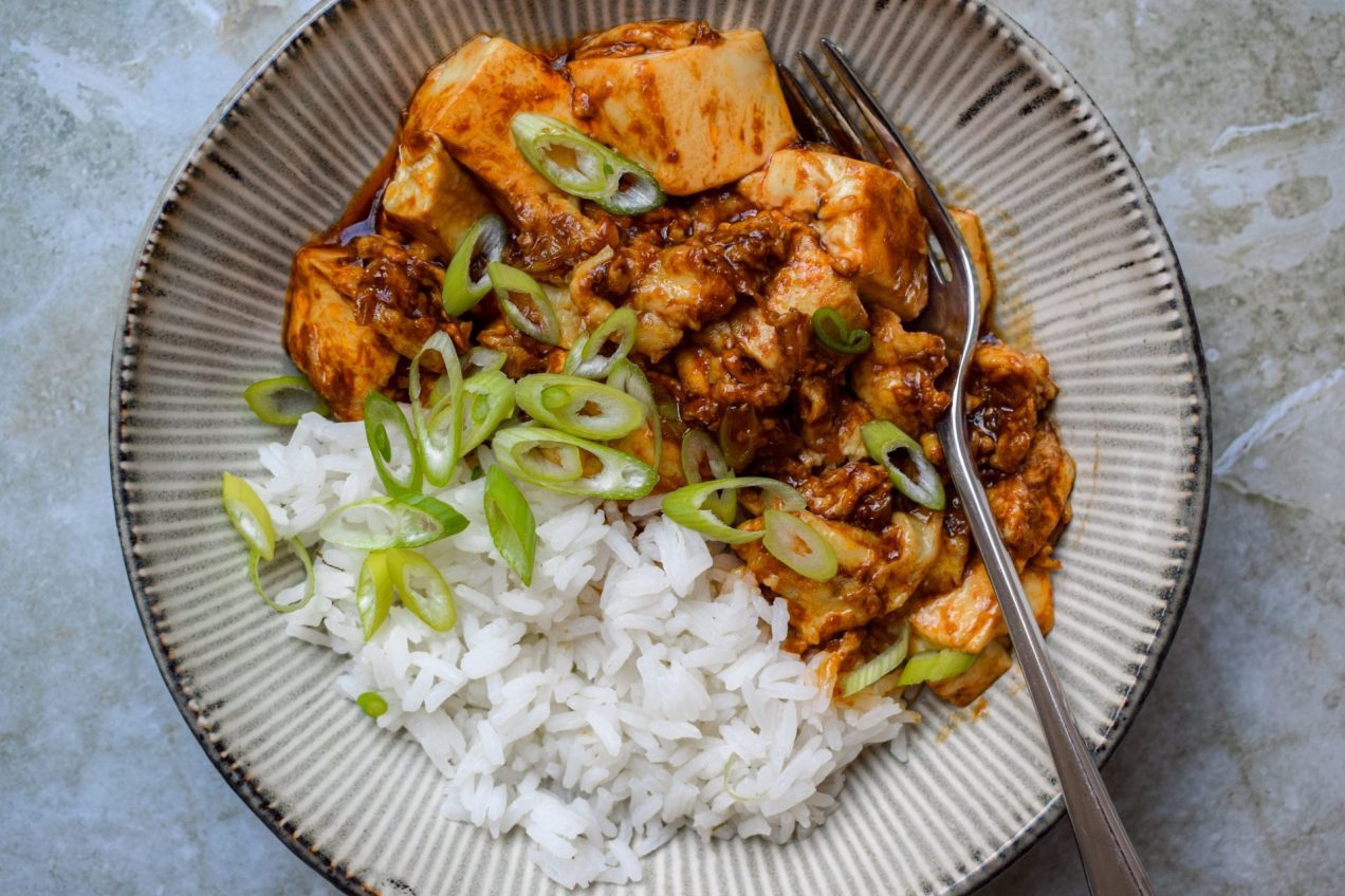 Close up of a grey bowl of tofu, eggs, white rice and spring onion slices.