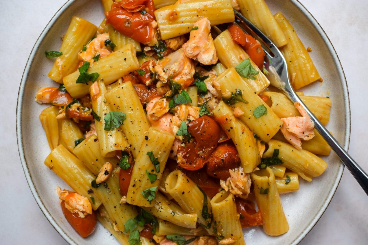 Plate of pasta with burst cherry tomatoes, shredded basil and flaked salmon,