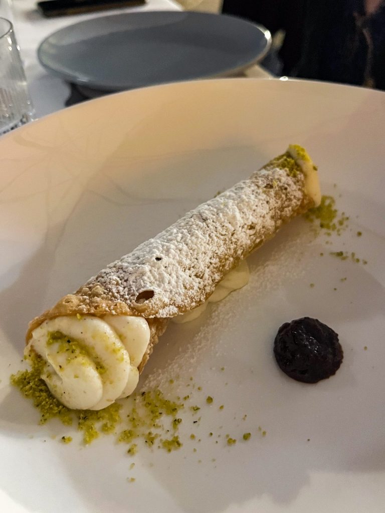 Canolo on a plate with ground pistachios and a small round dollop of carob jam.