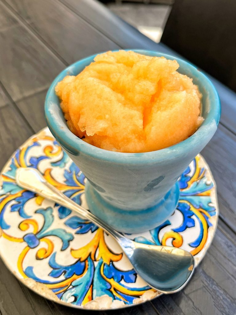 Melon granita in a frozen blue cup on a yellow, white and blue decorated plate.