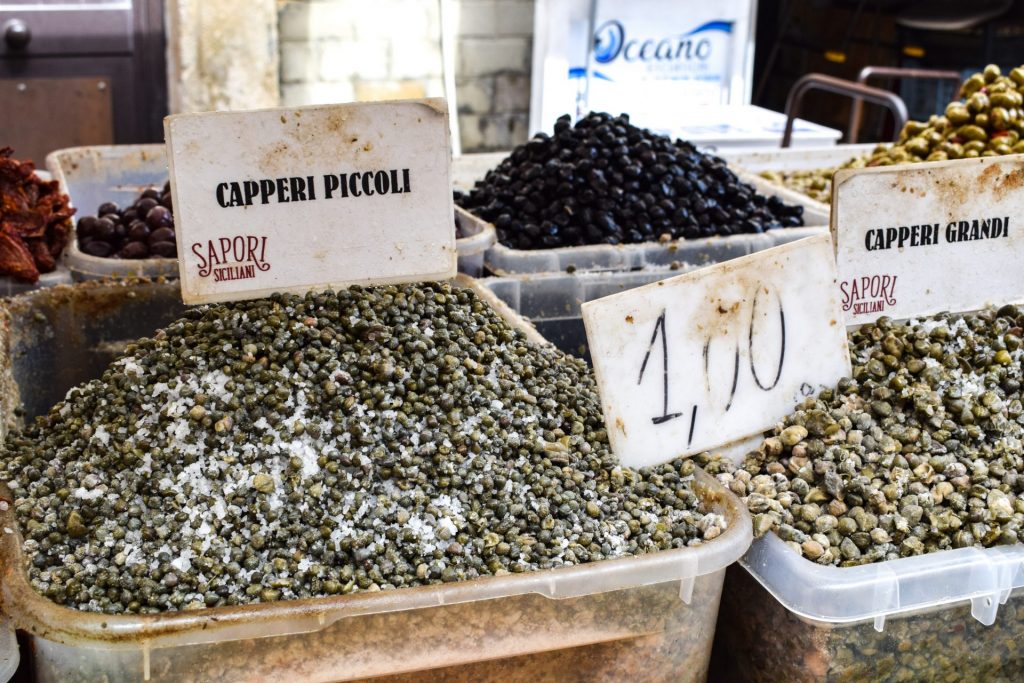 Plastic tubs of salted capers on a market stall.