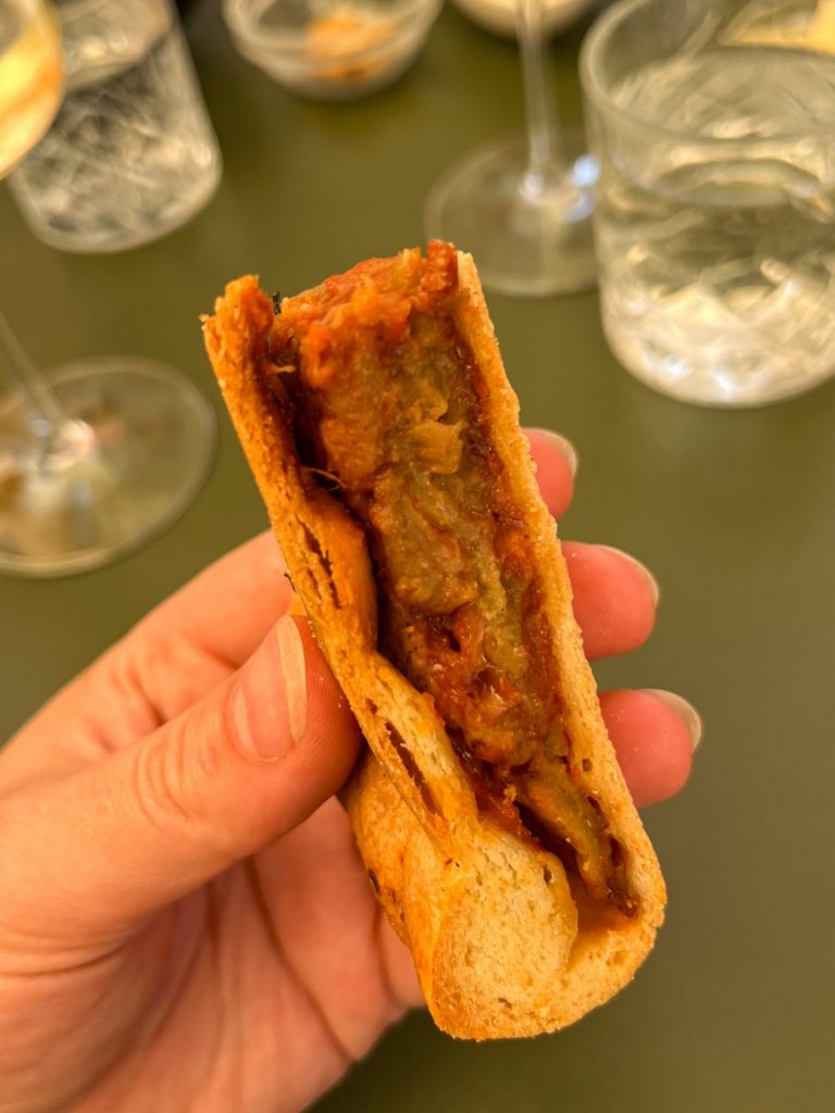 A hand holding up a caponata Scacciata to show the filling.