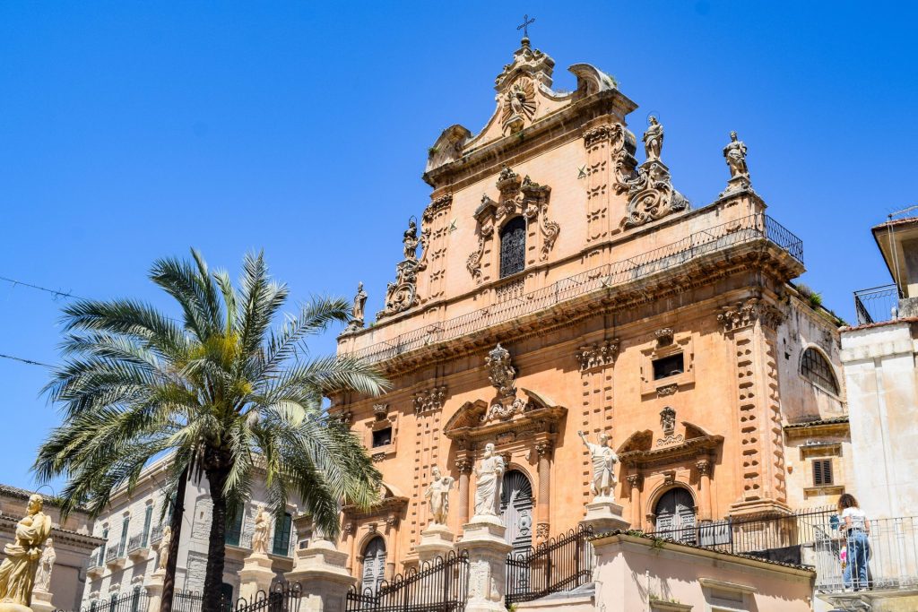 Baroque church with a palm tree outside it.