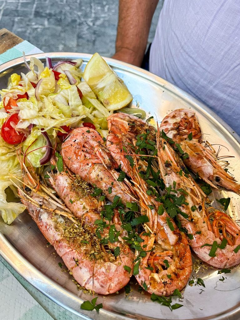 Metal platter of grilled whole prawns with a side salad.