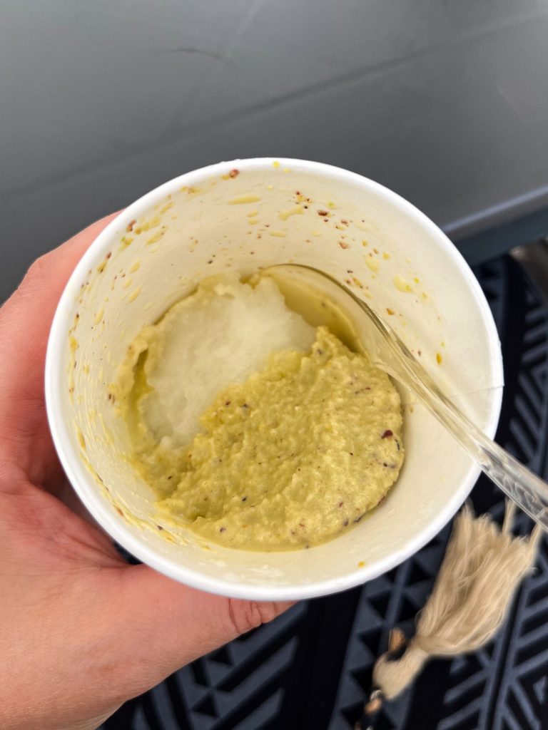 Hand holding a half eaten cup of lemon and pistachio granita.