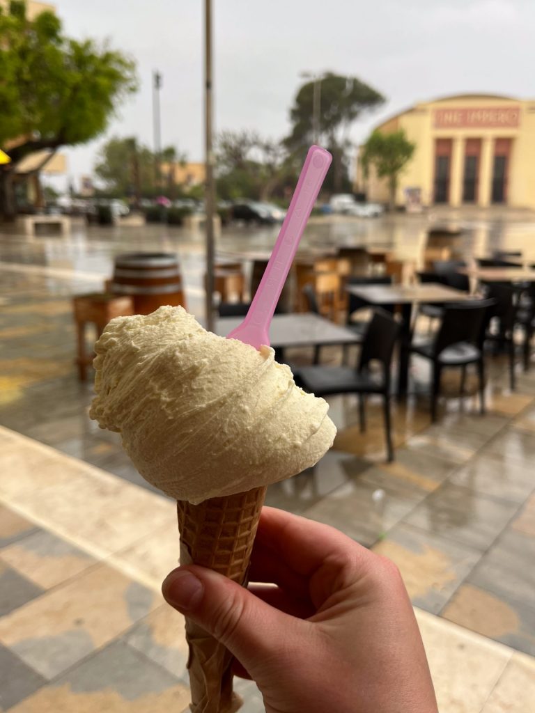 Hand holding a cone of marsala gelato with a pink plastic spoon