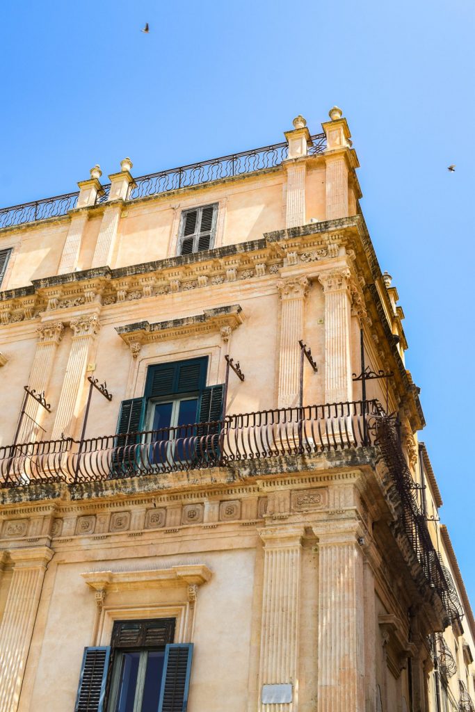 Swallows flying over the corner of a building in Noto.
