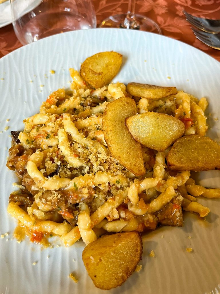 White plate of pasta Pesto alla Trapani with fried aubergine and potatoes.