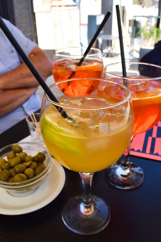Three spritz and a bowl of olives on a bar table.
