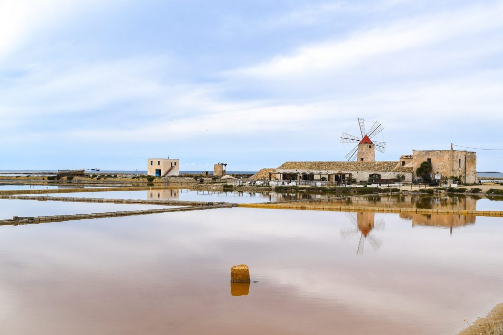 View of the Trapani salt flats tinged pink against a blue sky.