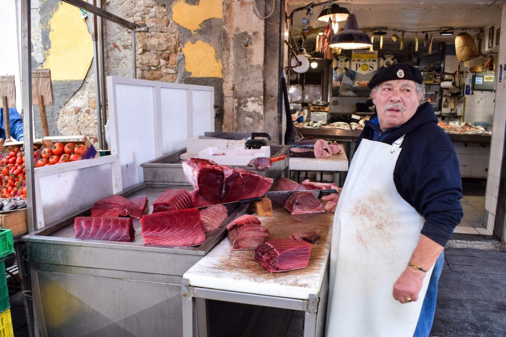 Fishmonger breaking down a tuna fish on a cutting board in the market.