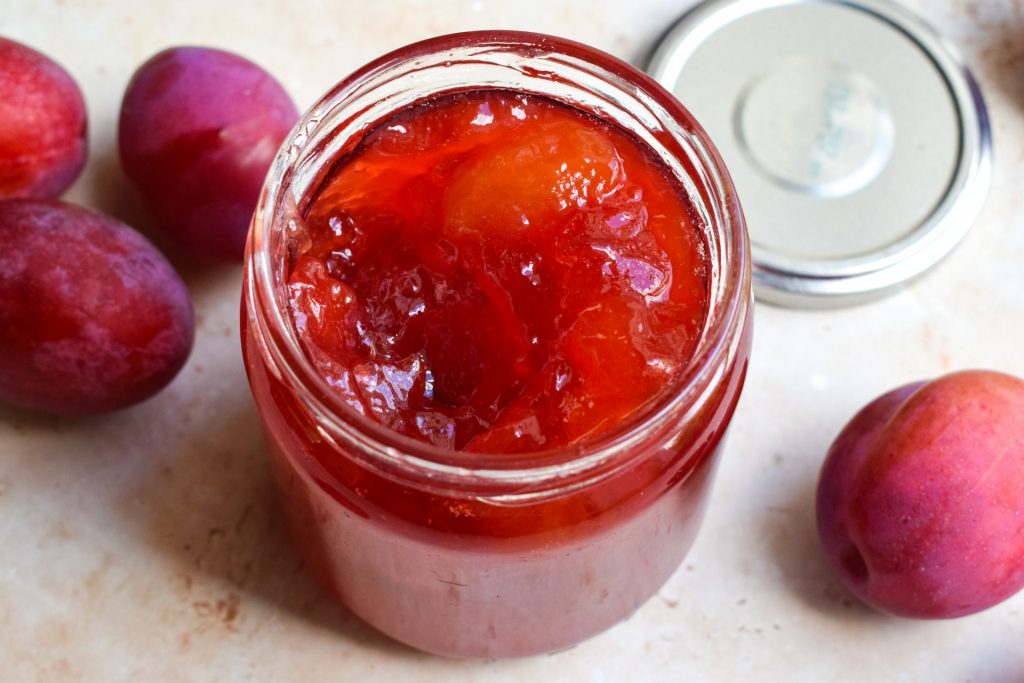Close up of an open jar of plum jam with whole plums next to it.