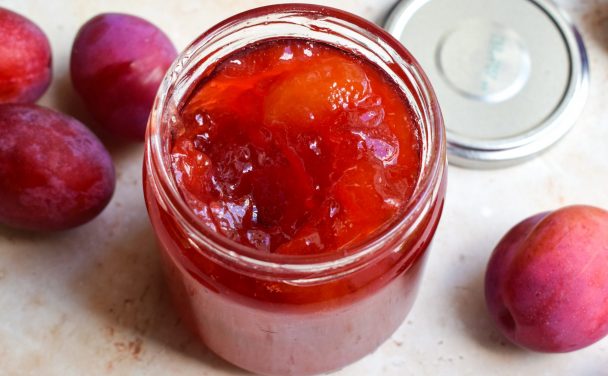 Close up of an open jar of plum jam with whole plums next to it.