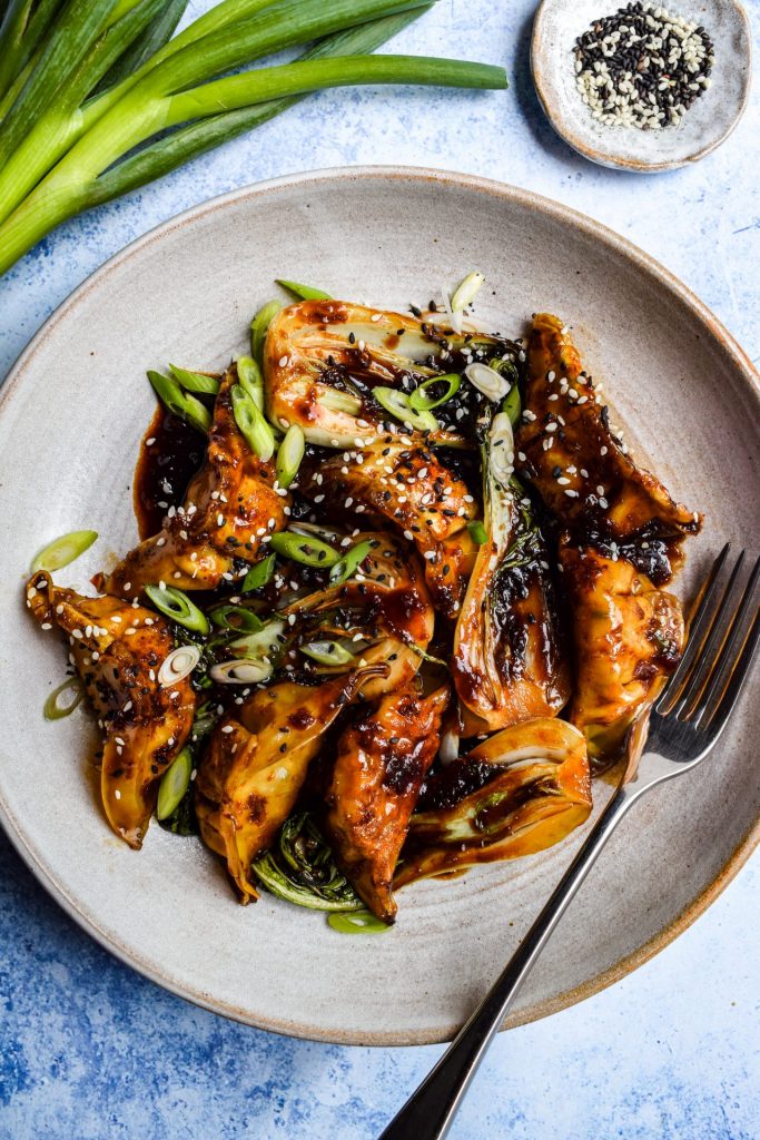 Close up of a dumpling and pak choi stir fry topped with sliced spring onions and toasted sesame seeds.