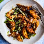 Bowl of dumplings in a dark stir fry sauce with cooked baby pak choi. Bowls of sesame seeds and a bunch of spring onions are on the side.
