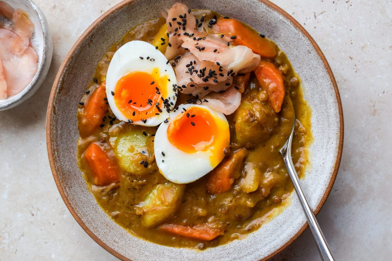 Bowl of Japanese lentil curry topped with a soft boiled egg, pickled ginger and black sesame seeds.