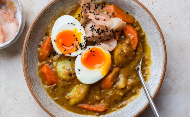 Bowl of Japanese lentil curry topped with a soft boiled egg, pickled ginger and black sesame seeds.