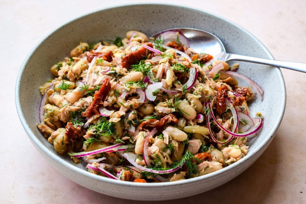 Bowl of tuna and white bean salad with a metal spoon.