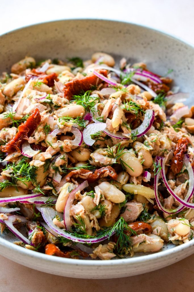 Close up of a tuna and white bean salad with red onions and sun-dried tomatoes.