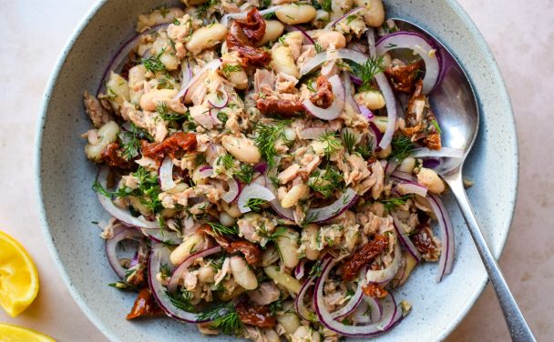 A grey bowl of tuna, white bean, fill, sun-dried tomato and red onion salad with lemon wedges on the side.