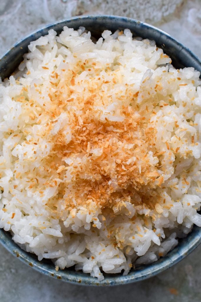 Close up of a bowl of Thai coconut rice topped with toasted coconut. 