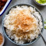 Bowl of coconut rice topped with toasted coconut with a spoon in the side.