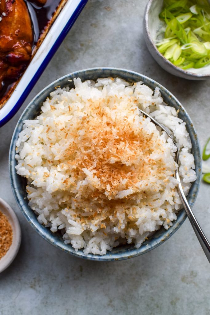 Bowl of coconut rice topped with toasted coconut with a spoon in the side.