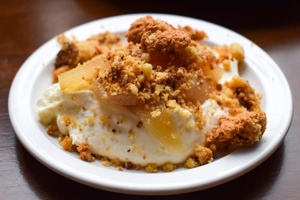 Sliced poached pears and crumbled amaretti biscuits on top of a plate of mascarpone. 